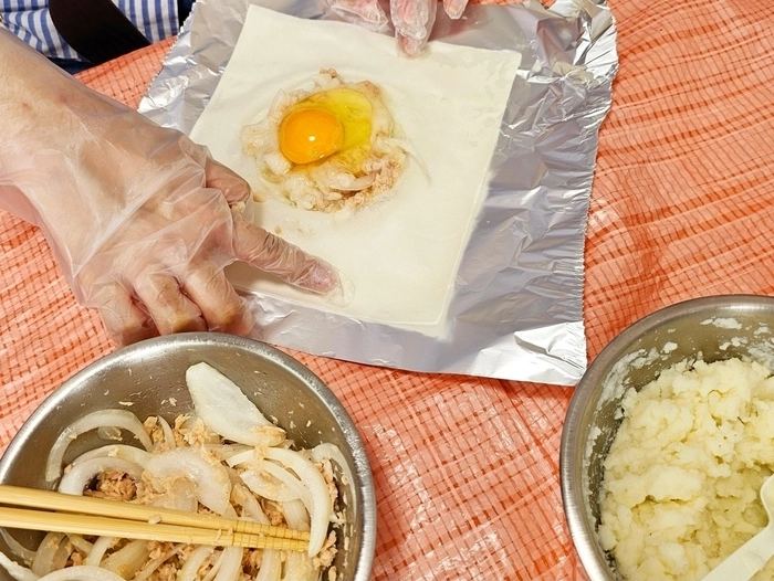 アフリカの伝統的な家庭料理のブルックの材料を春巻きの皮に慎重に包んでいる様子